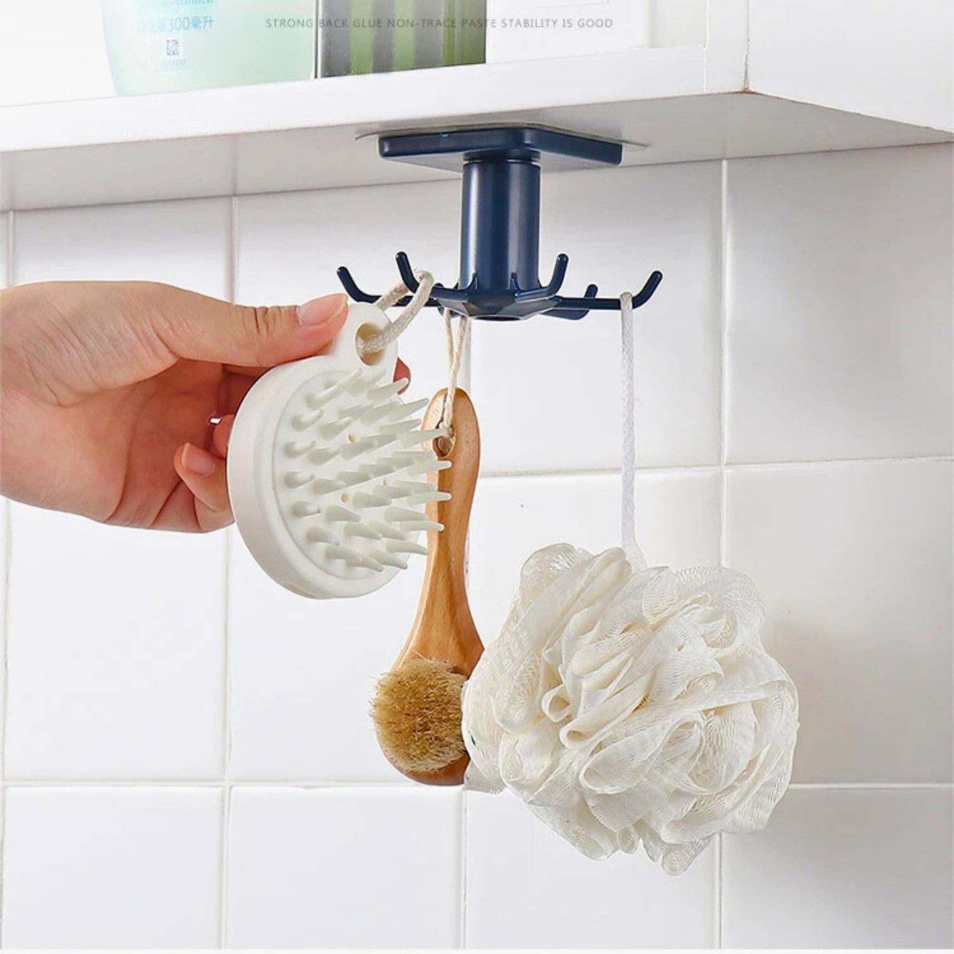 A bathroom organizer hook holding a sponge and a brush, mounted on a white tiled wall